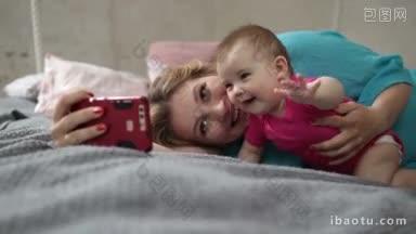 快乐的年轻妈妈和可爱的婴儿躺在床上用智能手机自拍，微笑的妈妈和可爱的婴儿
